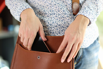 Woman in casual clothes holds her smartphone in her shoulder bag.