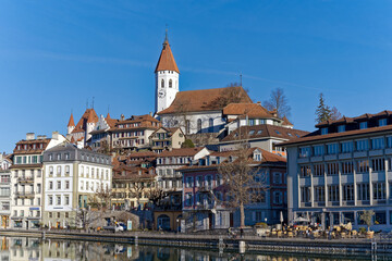 Naklejka premium Old town of City of Thun with church and castle on a hill in the background on a sunny winter day. Photo taken February 21st, 2023, Thun, Switzerland.