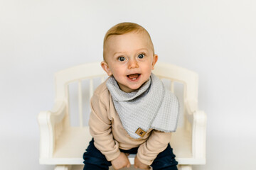 Lachender kleiner Junge in neutralen Farben sitzt auf wei&szlig;er Holzbank