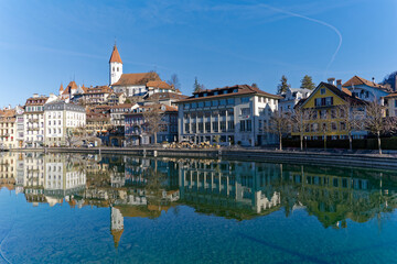 Fototapeta premium Scenic view of Aare River with the old town of Swiss City of Thun and castle and church on a hill on a sunny winter day. Photo taken February 21st, 2023, Thun, Switzerland.