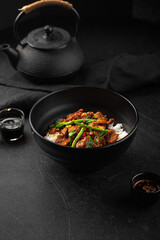 Asian cooked beef with spring onion and rice on black background