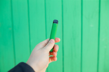 Man holding green electronical cigarette vaping pen on green wooden door background