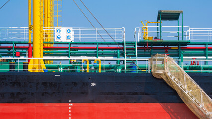 Obraz premium Background of Oil pipeline system with gangway accommodation ladder of red and black oil tanker while moored at harbor against blue sky 