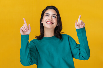 Beautiful smiling woman pointing up over yellow background.