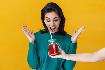 Pleasantly surprised girl by giving him a smoothie isolated on yellow