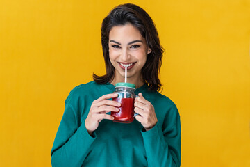 Smiling woman drinking red smoothie isolated on yellow.