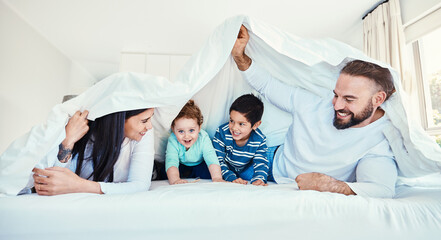 Family, blanket and fun by children and parents in bed, happy and smile while playing and bonding in their home. Bedroom, fort and kids with mother and father, waking up and enjoying weekend indoors