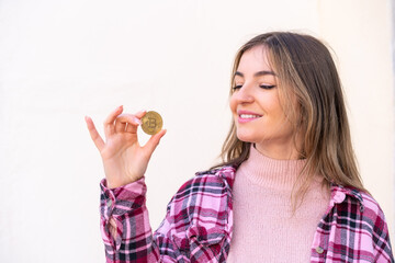 Young pretty Romanian woman holding a Bitcoin at outdoors with happy expression