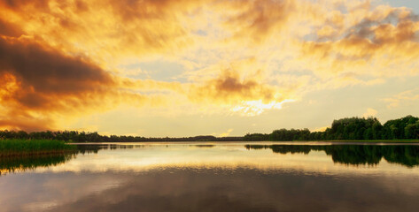 Lake landscape in the evening. A view of a lake with thick, sun-tinged yellow clouds