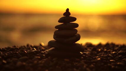 Balanced rock pyramid on pebbles beach. Golden sea bokeh on background. 