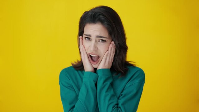 Video of urprised young woman screaming and putting her hands on her face looking at camera isolated on yellow