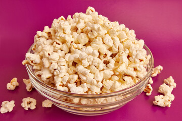 A bowl on a pink background is completely filled with popcorn. A sweet snack.