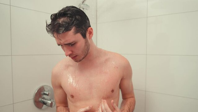 Young man taking a cold shower to stimulate circulation and promote health, feeling chilly but invigorated.