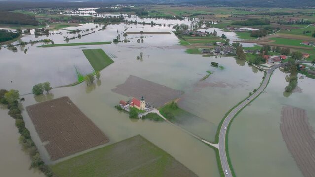 AERIAL: Church on a dry island in the middle of large area of flooded fields. Extensive flooding of farmland after a rising river overflowed its banks. Autumn flood in rural area after heavy rainfall.