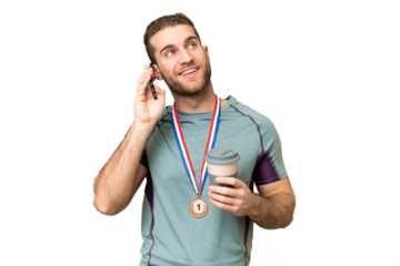 Young handsome blonde man with medals over isolated chroma key background holding coffee to take away and a mobile