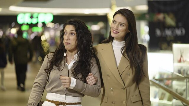Medium shot of two happy female friends walking through the shops of shopping mall in slow-motion