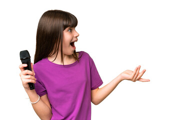 Little singer girl picking up a microphone over isolated background with surprise facial expression
