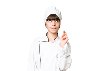 Little caucasian chef girl over isolated background with fingers crossing and wishing the best