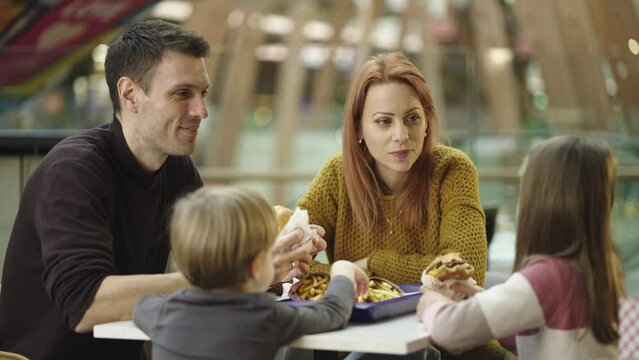 Slow-motion shot of a happy affectionate family enjoying snacks and drinks in a caf� of shopping mall