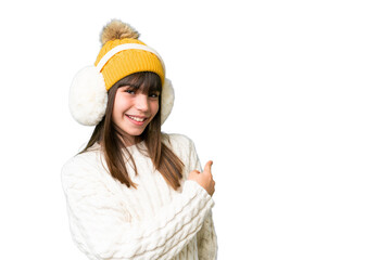 Little caucasian girl wearing winter muffs over isolated background pointing back