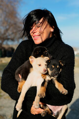Naklejka na ściany i meble a girl of thirty is holding homeless puppies in her hands, a woman is a volunteer she helps the puppies,takes care of them,takes a photo for them to attach the puppies to families. national puppy day