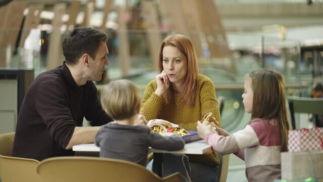 Cheerful parents and kids eating together and talking with each other at caf� in shopping mall. Shot in slow-motion