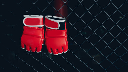 Red Gloves for MMA Boxers fighter hang on ring octagon black wall. Concept sport banner - obrazy, fototapety, plakaty
