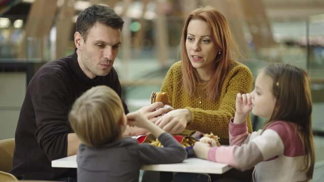 Family lunch with children in restaurant. Father, mother and two daughters eating burgers and french fries at caf� restaurant in slow-motion