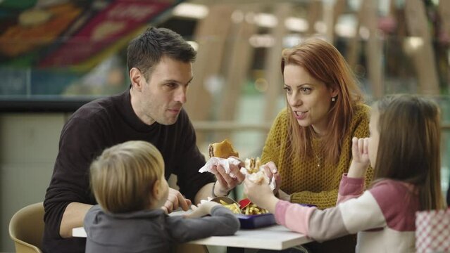Family eating fast food at caf�. Parents with kids eating french fries and burger together at caf� in slow-motion