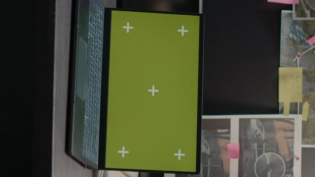 Vertical video: Modern laptop with greenscreen placed on archive desk in police evidence room, blank mockup template on pc. Wireless computer showing isolated chroma key copyspace, incident room.