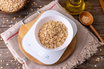 Oatmeal in a white bowl on the kitchen scales on wooden background, rustic style, top view