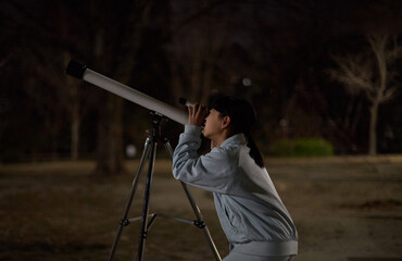 春の夜の公園で天体望遠鏡を使って観察している小学生の女の子の様子