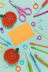 Blue background with crochet pumpkin, crochet tools and yellow paper blank. Copy space.