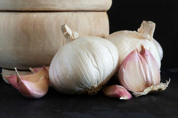 Natural antibiotic,Several garlic cloves and garlic next to a wooden mortar and isolated on a black background