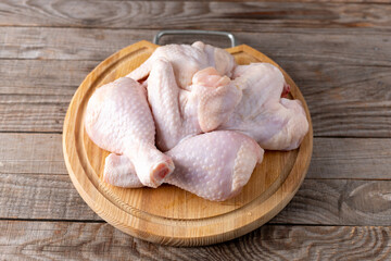 Raw chicken wings and drumsticks on cutting board on wooden table.