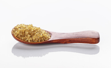 coarse yellow sea salt in a wooden spoon, isolated on a white background with reflection