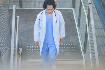病院の階段を歩くスクラブ白衣を着た若い男性医師