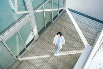 病院の廊下を歩くスクラブ白衣を着た若い男性医師