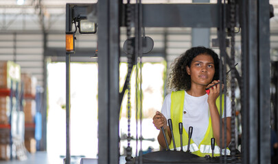 Multiracial female warehouse worker driving forklift truck in distribution storehouse. Woman vehicle driver working in shipping storage factory lifting, moving and unloading cargo ready for delivery.