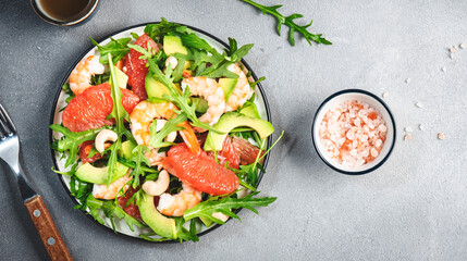 Seafood salad with shrimps, avocado, grapefruit, arugula and cashews. Gray stone kitchen  table background, top view