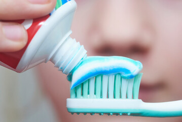 Child girl squeezes toothpaste on a toothbrush during the morning toilet, close-up