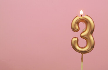 Burning gold birthday candle on pink background, number 3. Large copy space for text.