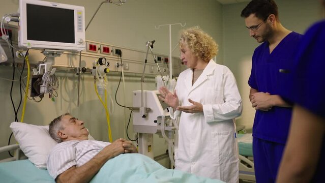 Senior patient lying in the bed, talks with doctor and nurse in hospital. Modern hospital ward in slow-motion