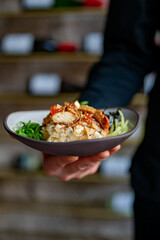 chef holding delicious donburi bowl with fish, rice and vegetables