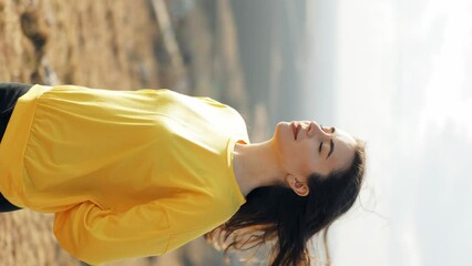 Portrait of a long-haired brown-haired woman enjoying nature in the field. Attractive woman touches her long hair, wind blows her hair. Happy look, feeling of freedom. Vertical video orientation - Powered by Adobe