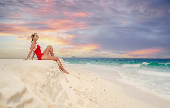 Vacation on the seashore.Young woman in red swimsuit sitting on the beautiful tropical white sand beach.