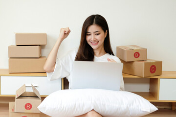 Startup SME small business entrepreneur of freelance Asian woman using a laptop with box Cheerful success Asian woman her hand lifts up online marketing packaging box and delivery SME idea concept.