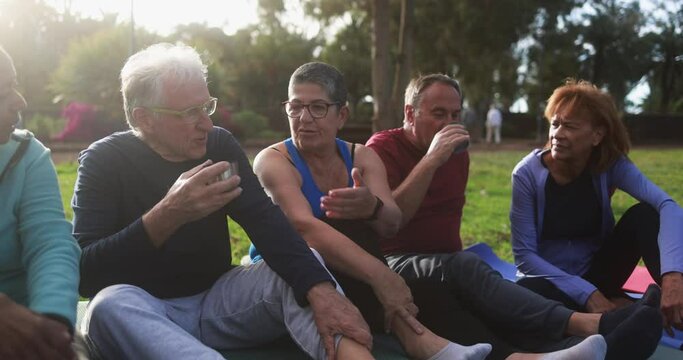 Multiracial senior people having fun drinking hot tea after workout exercises outdoor with city park in background - Healthy lifestyle and joyful elderly lifestyle concept