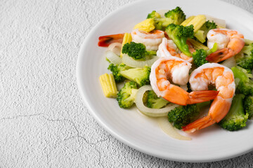 Fried broccoli and shrimp with oyster sauce, onion and corn in white dish on concrete table.
