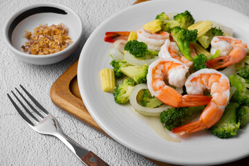 Fried broccoli and shrimp with oyster sauce, onion and corn in white dish on concrete table.